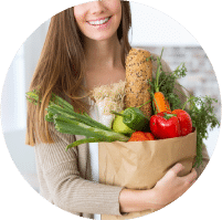 תמונת אווירה לקטגוריית התזונה. בתמונה אישה מחייכת המחזיקה שקית נייר חומה גדולה ובתוכה מגוון ירקות טריים ומבריקים עם צבעים חזקים ובוהקים.