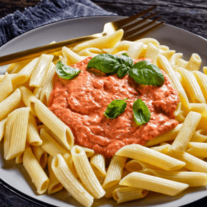 תמונה של צלחת עם פסטה ועליה רוטב רוזה וורדרד, מקושט בעלי בזיליקום ולצד המנה מונח מזלג מוזהב